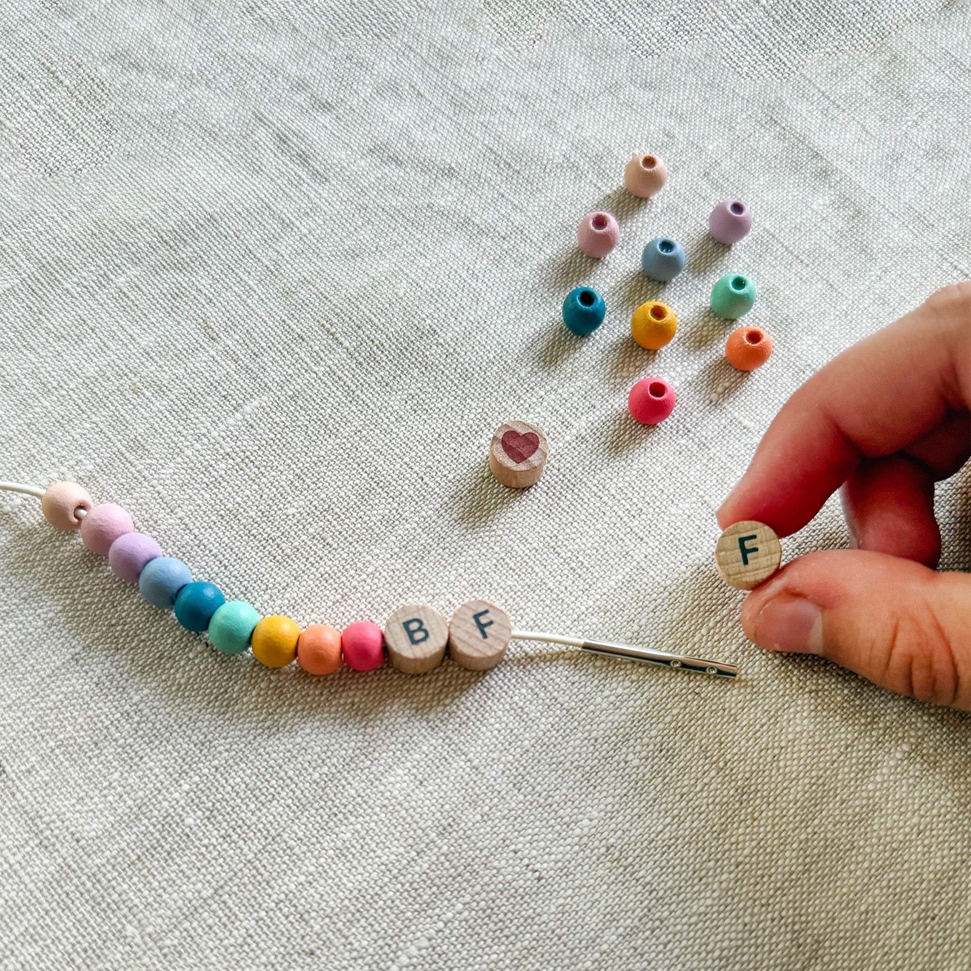 Child threading beads onto elastic cord, creating a "BFF" friendship bracelet.