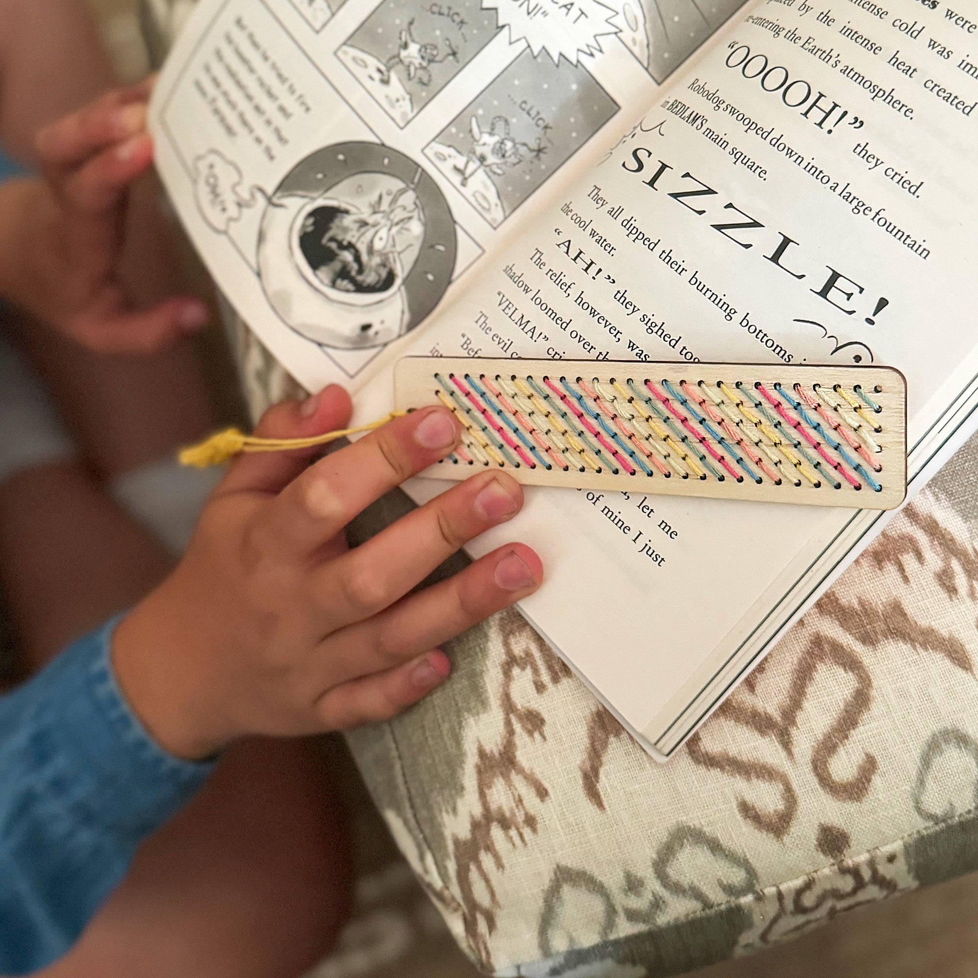 Child using cross-stitched wooden bookmark in a book