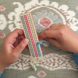 Child stitching a pattern onto the wooden bookmark using pastel thread.
