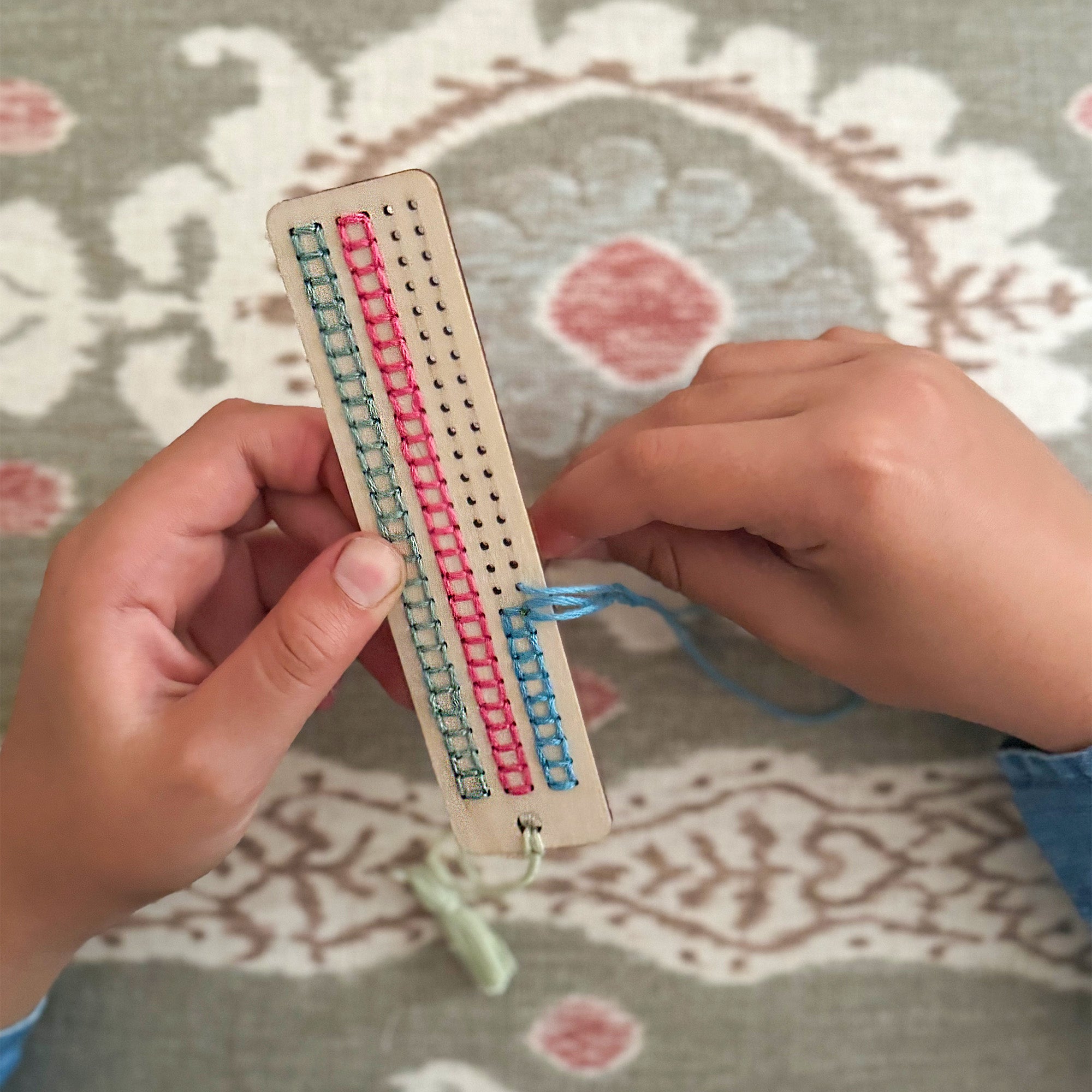 Child stitching a pattern onto the wooden bookmark using pastel thread.