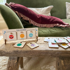 Cotton Twist wooden feelings chart on a table with "excited," "proud," and "calm" tokens, and others scattered nearby.