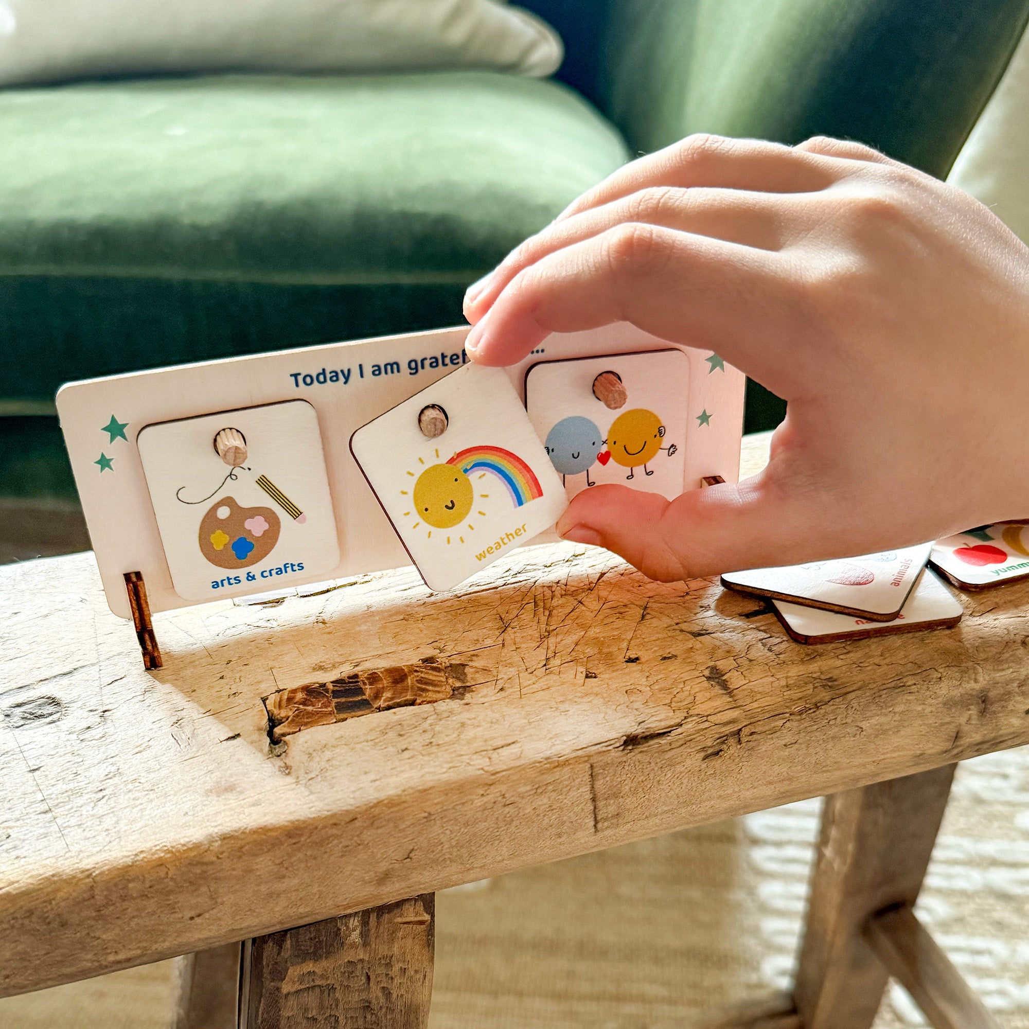Child selecting a wooden gratitude token to place on a “Today I am grateful for…” chart with colourful illustrations.