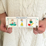 Child holding wooden gratitude chart with three tokens slotted in