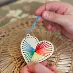 Child stitching a pattern onto the wooden heart keyring using colourful thread.