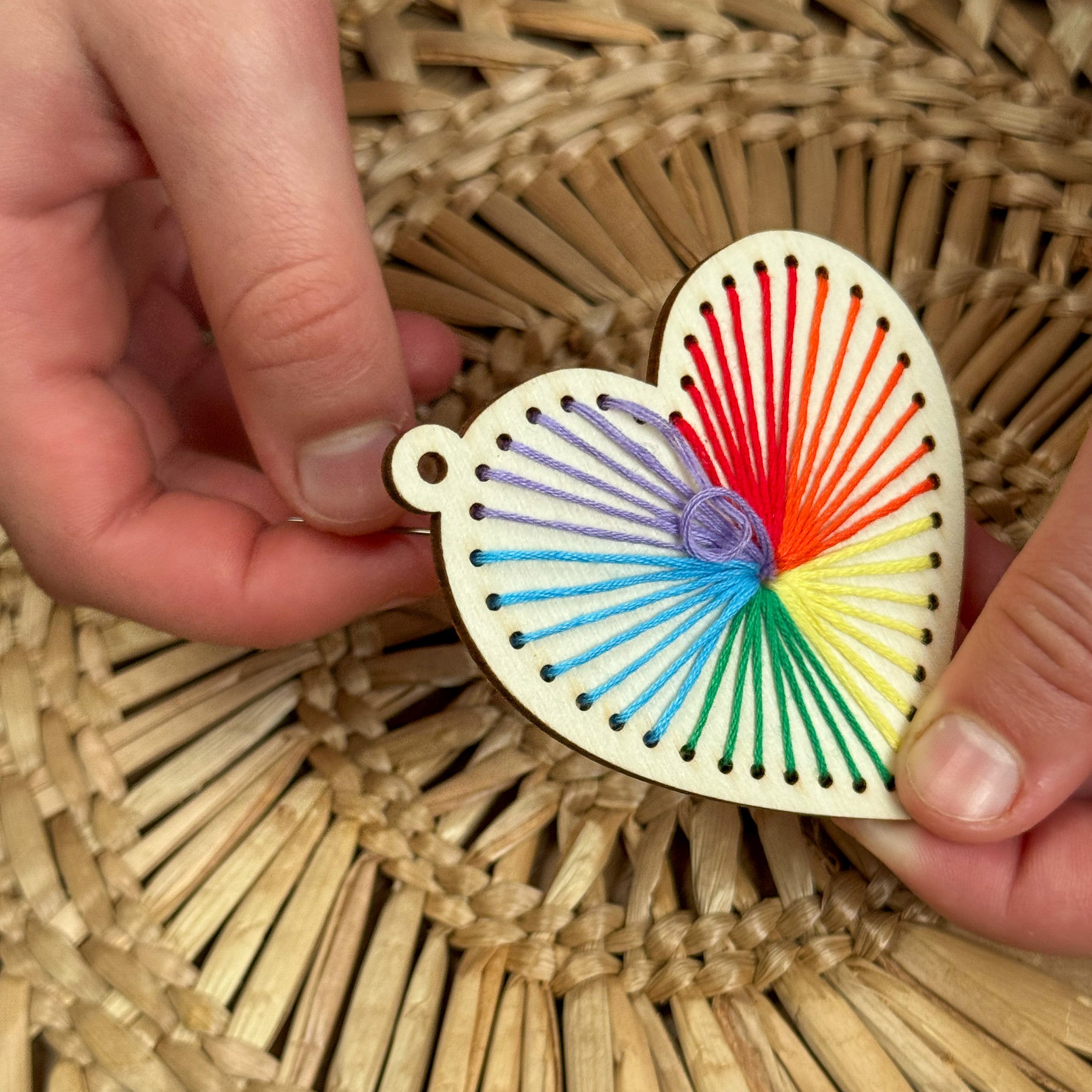 Child stitching a pattern onto the wooden heart keyring using colourful thread.