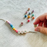 Child threading beads onto elastic cord, creating a "KIND" friendship bracelet.