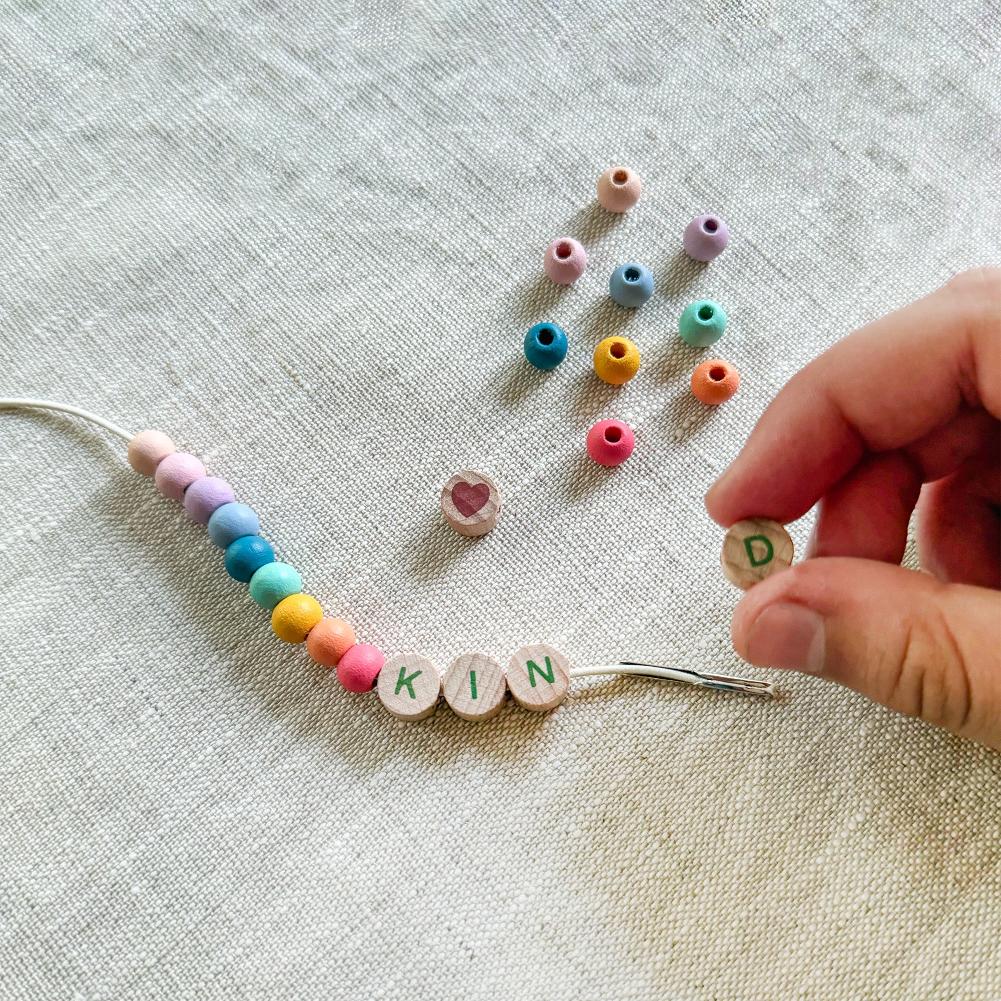 Child threading beads onto elastic cord, creating a "KIND" friendship bracelet.