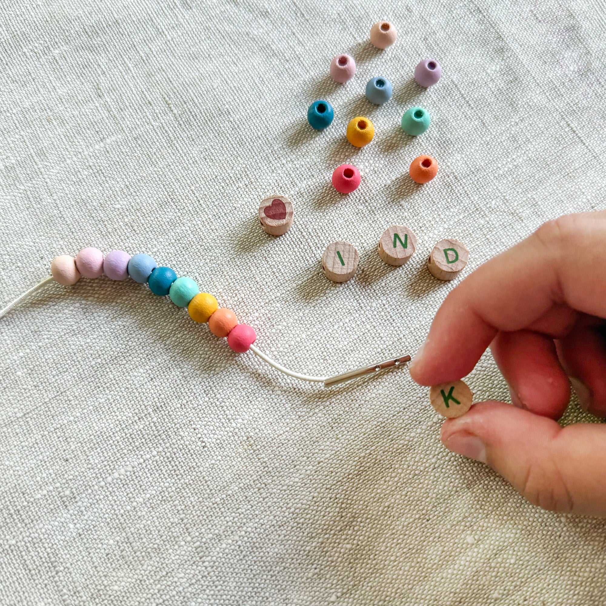 Child threading beads onto elastic cord, creating a "KIND" friendship bracelet.
