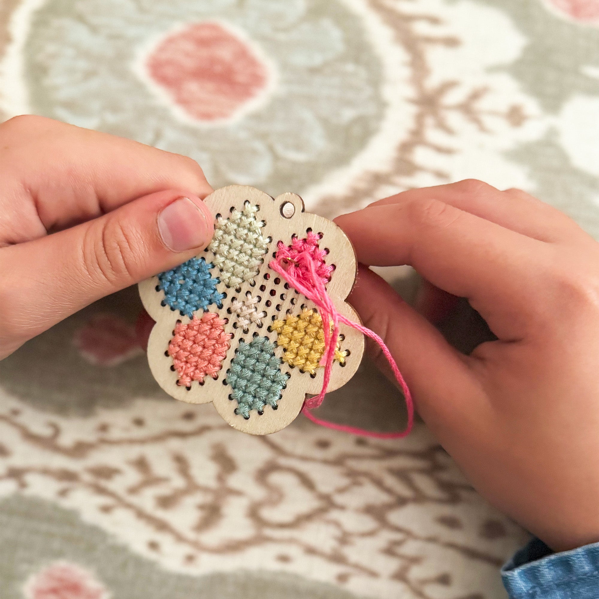 Child stitching a pattern onto the wooden flower keyring using pastel thread.