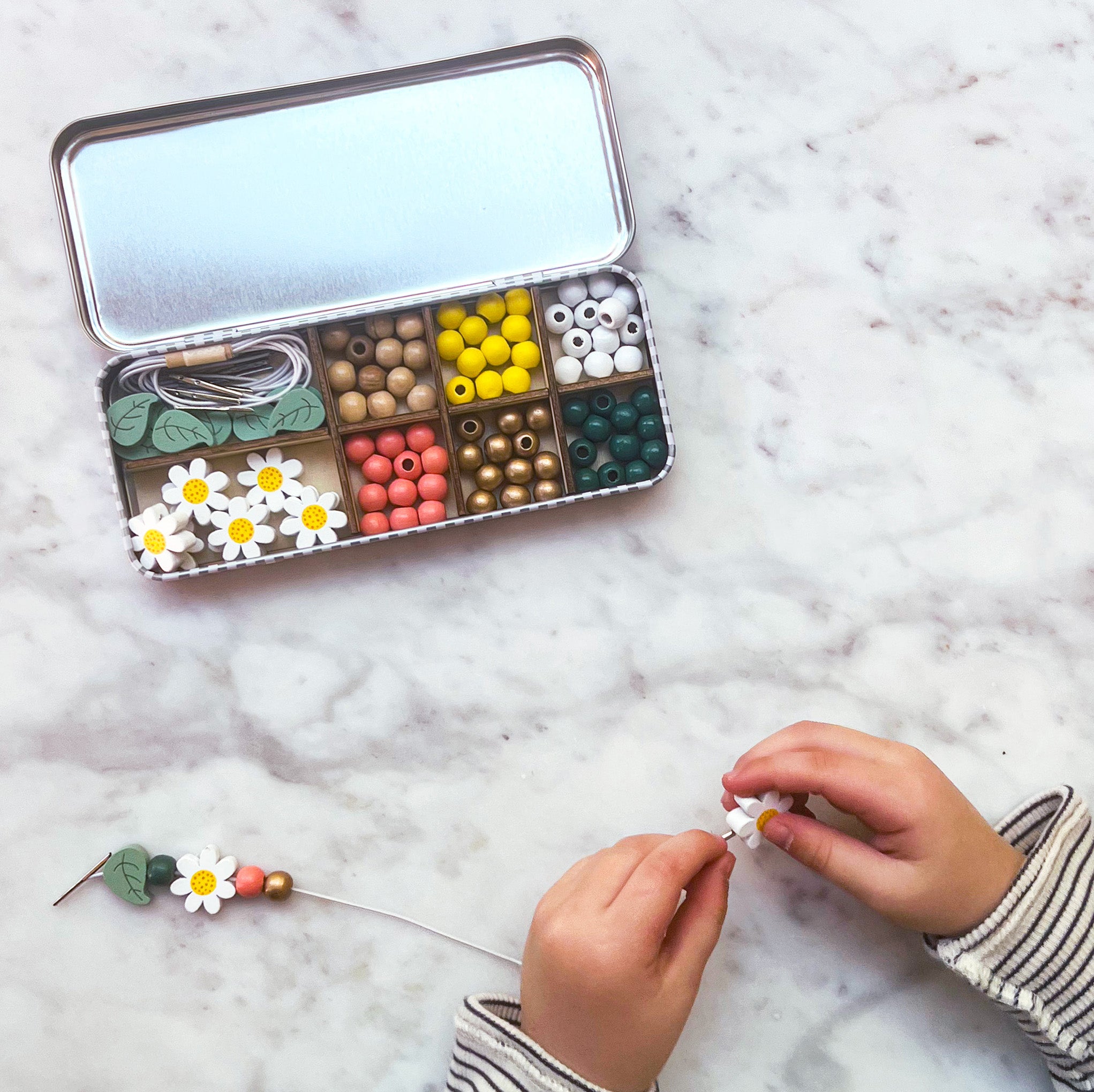 Child threading beads onto elastic cord, creating a bracelet from the daisy beading kit.