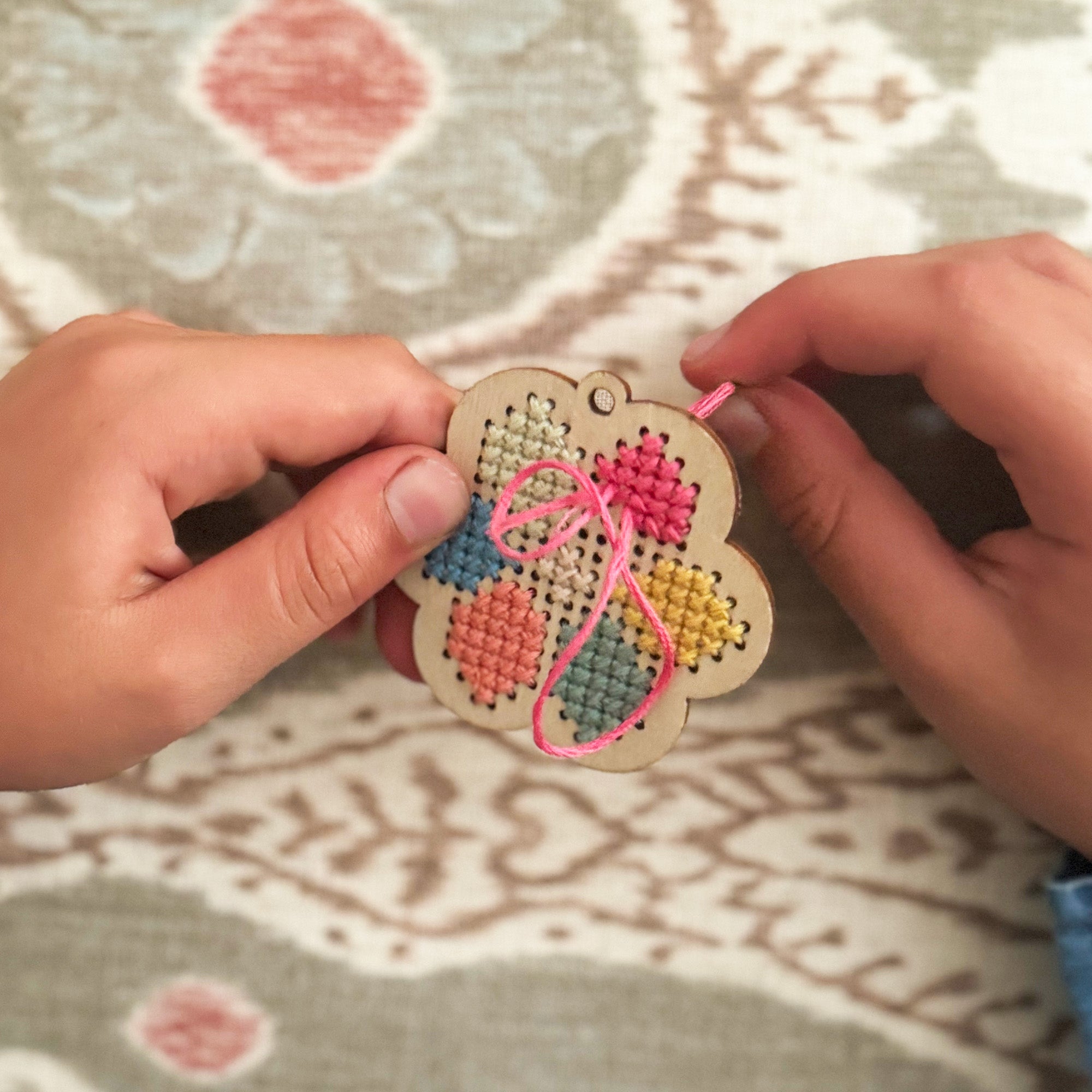 Child stitching a pattern onto the wooden flower keyring using pastel thread.