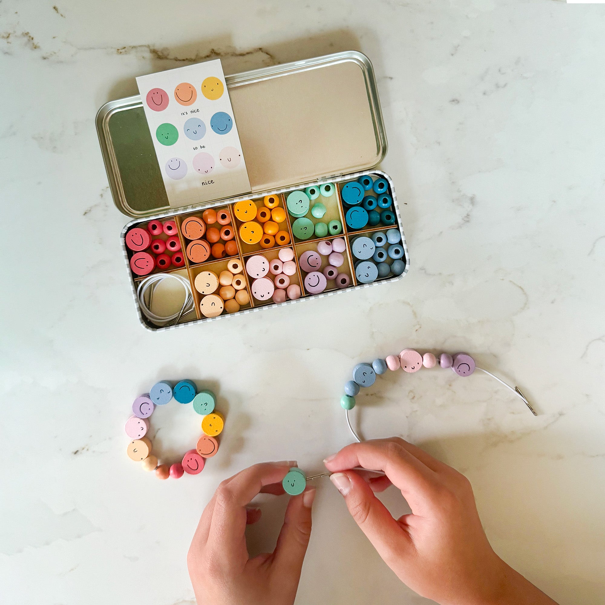Child threading beads onto elastic cord, actively engaged in creating a bracelet from the kit.