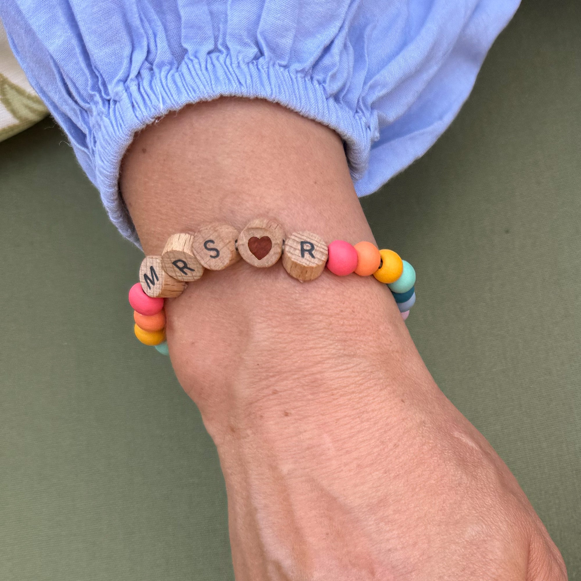 Bracelet on wrist with colourful beads and "MRS R" spelled in wooden beads with a heart bead in the centre.