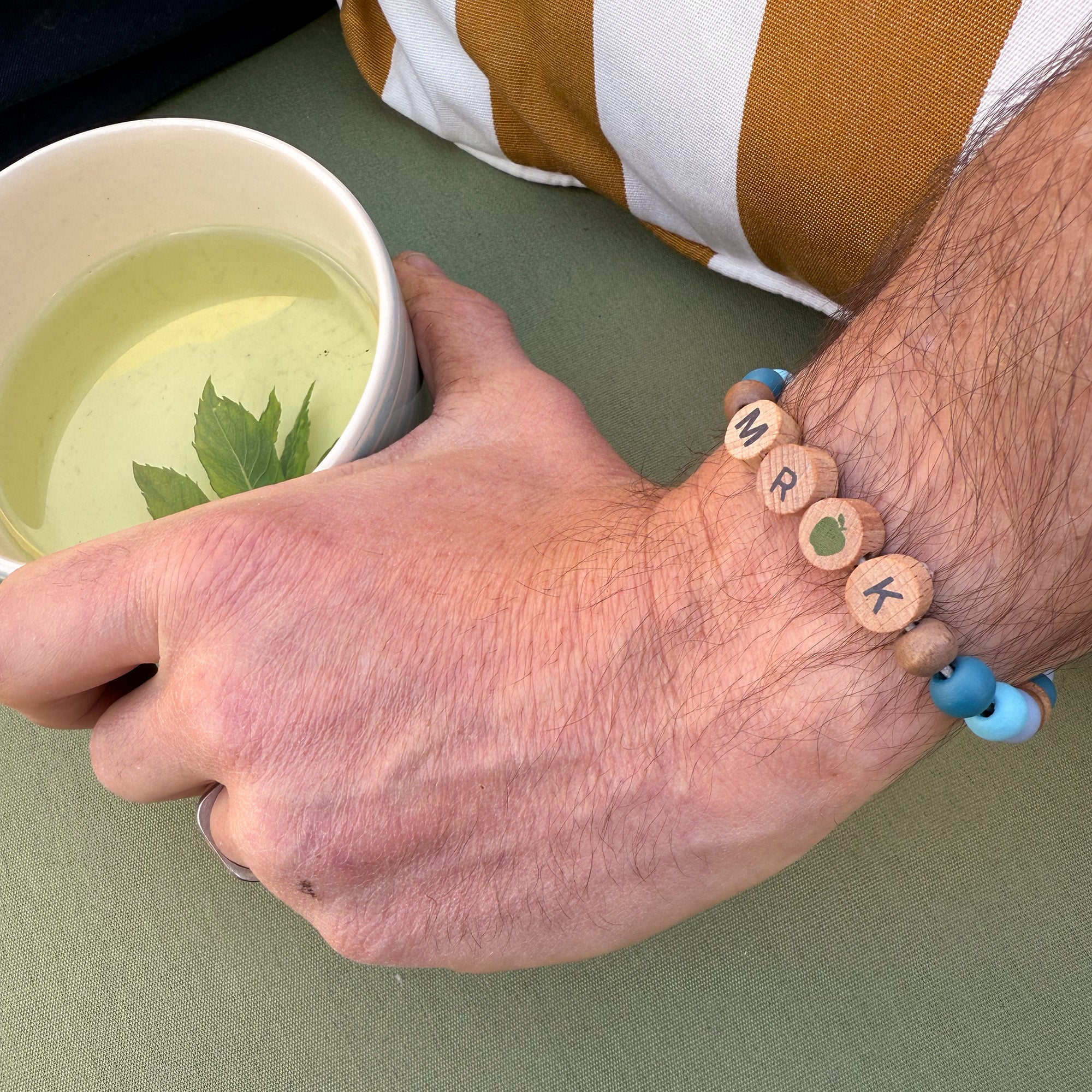 Bracelet on wrist with colourful beads and "MR K" spelled in wooden beads with an apple bead in the centre.