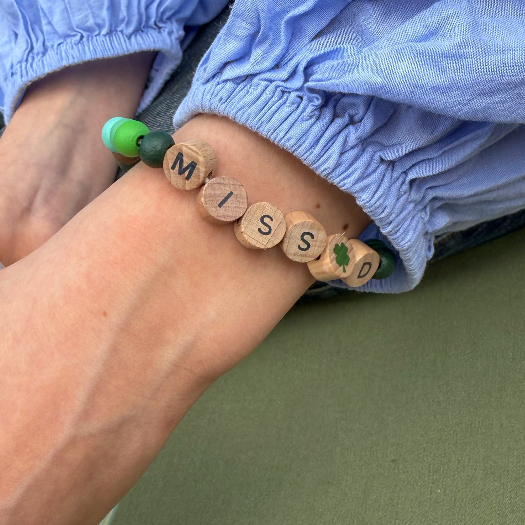 Bracelet on wrist with colourful beads and "MISS D" spelled in wooden beads with a clover bead in the centre.
