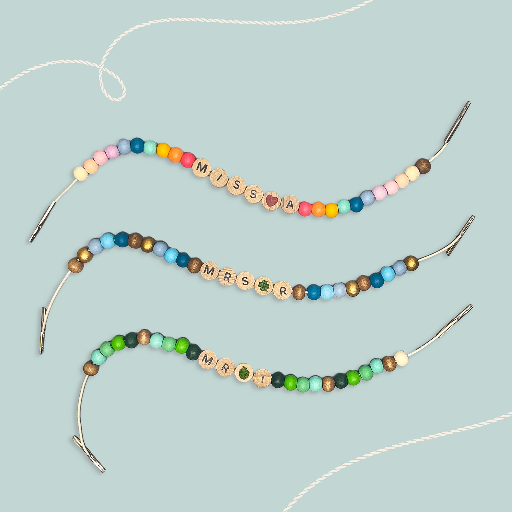 Three colourful beaded bracelets on a pale blue background, each with a teacher's prefix and initial spelled out in wooden beads.