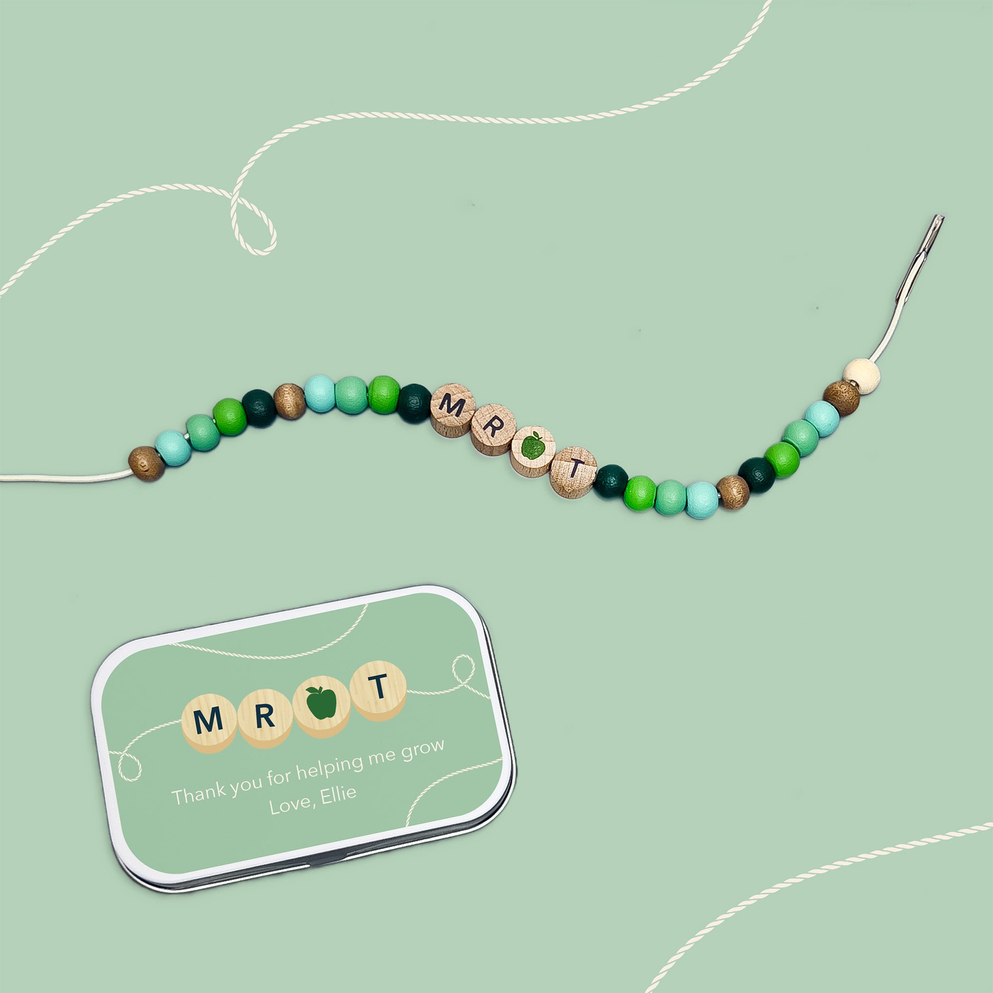Bracelet with "MR T" and green apple bead beside a matching personalised tin on a green background.