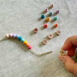 Child threading beads onto elastic cord, creating a "XOXO" friendship bracelet.