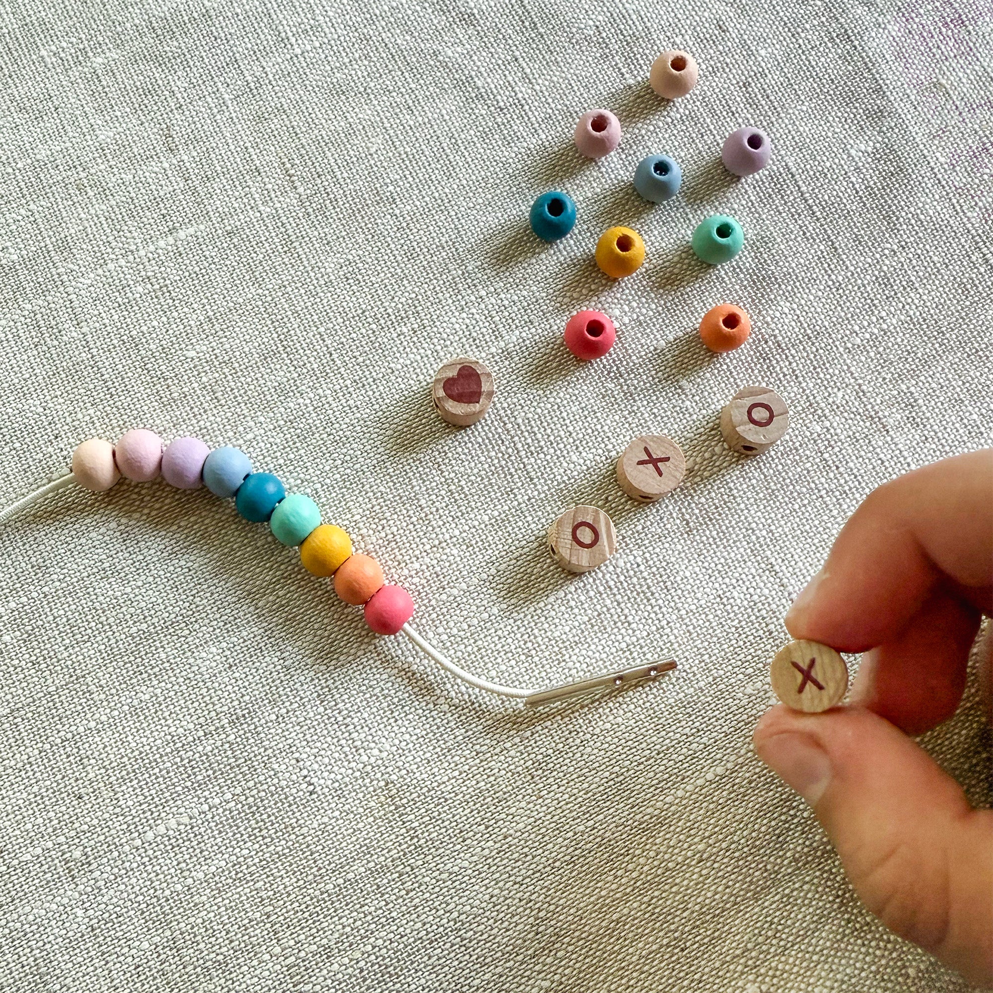 Child threading beads onto elastic cord, creating a "XOXO" friendship bracelet.