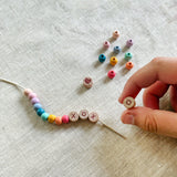 Child threading beads onto elastic cord, creating a "XOXO" friendship bracelet.