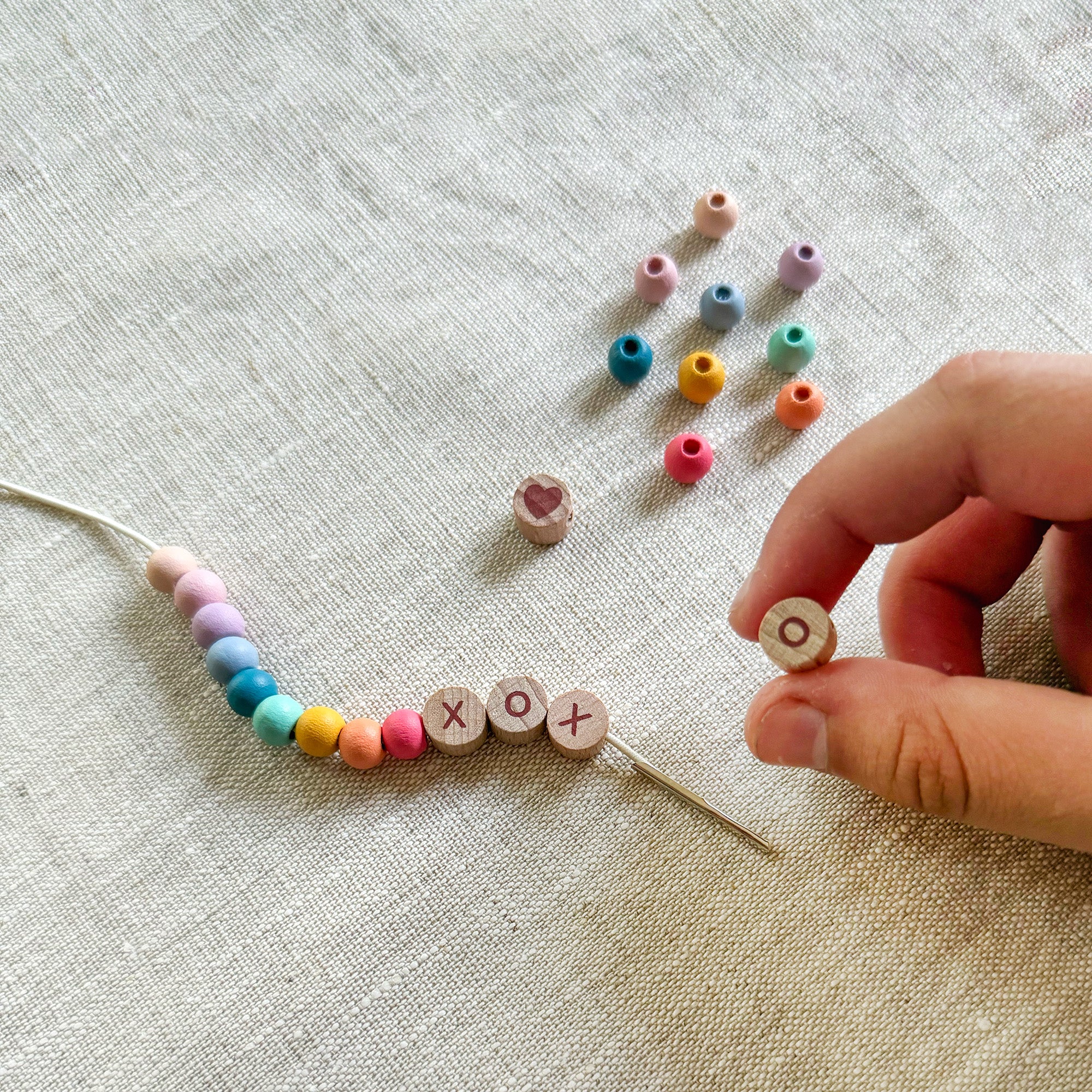 Child threading beads onto elastic cord, creating a "XOXO" friendship bracelet.