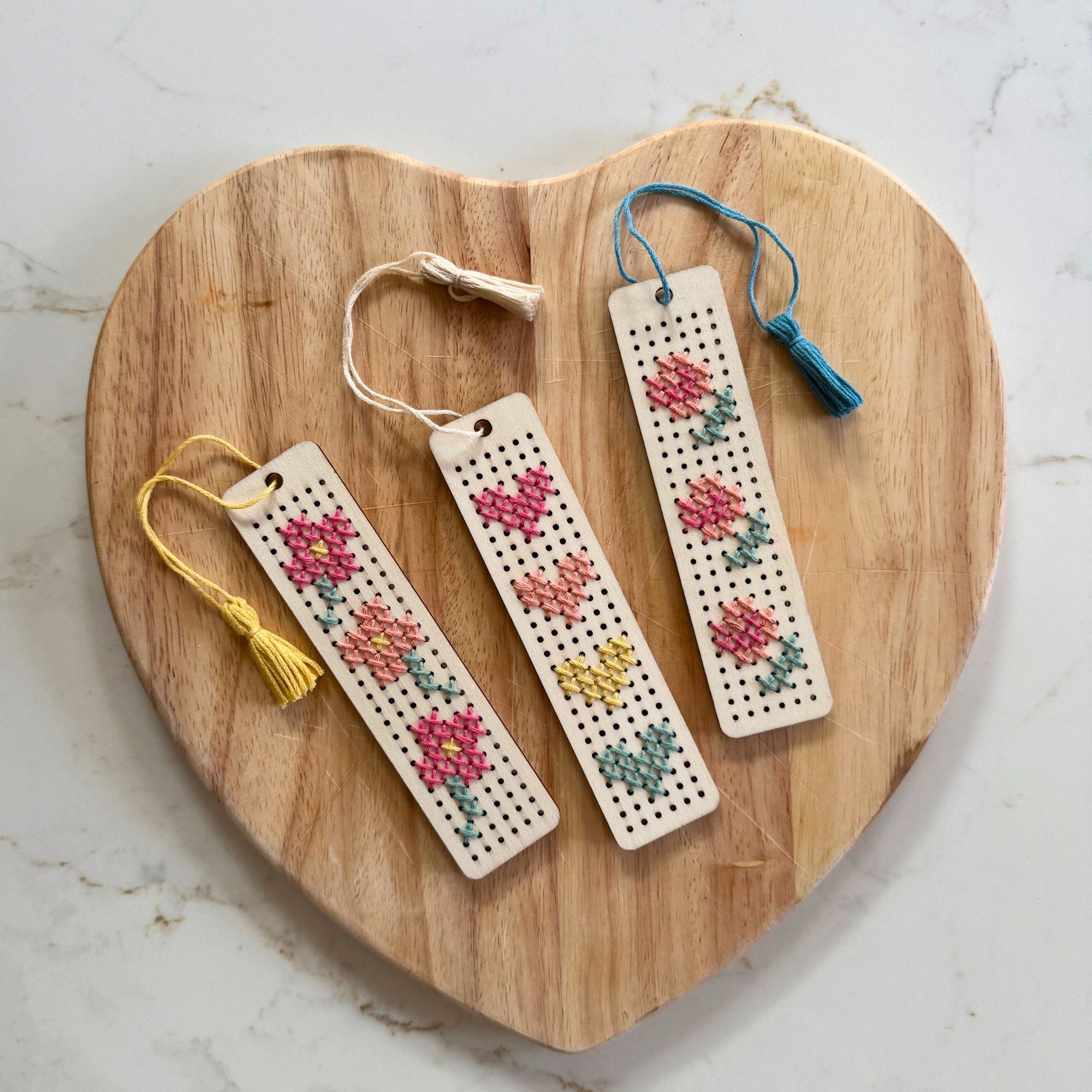 3 finished wooden bookmarks with stitched floral patterns and colourful tassels attached.