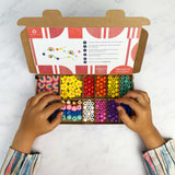 Child’s hands choosing beads from an open rainbow bracelet kit with instruction card.