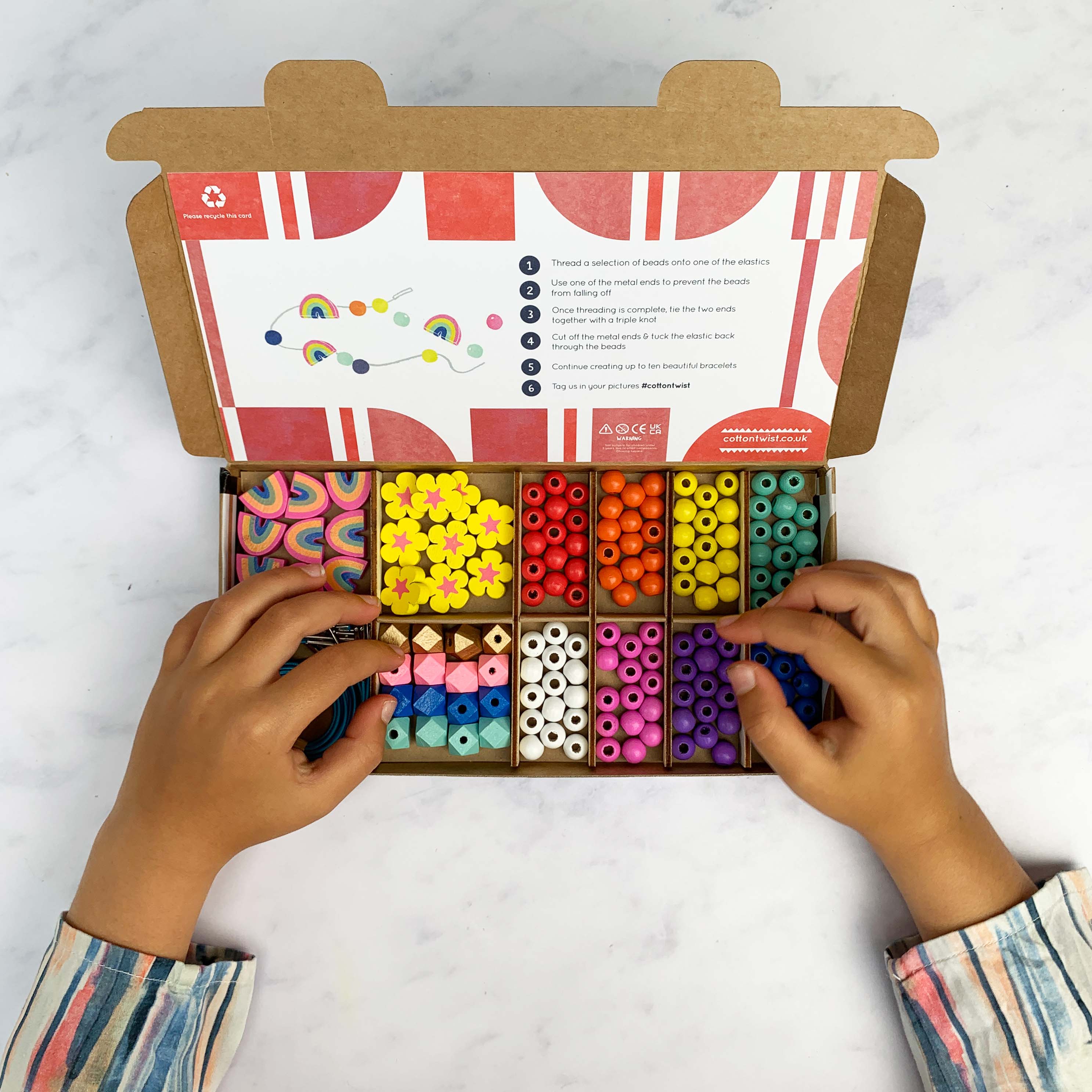 Child’s hands choosing beads from an open rainbow bracelet kit with instruction card.