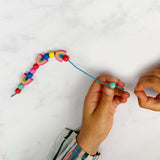 Child threading colourful beads, including rainbows, onto a blue elastic cord.