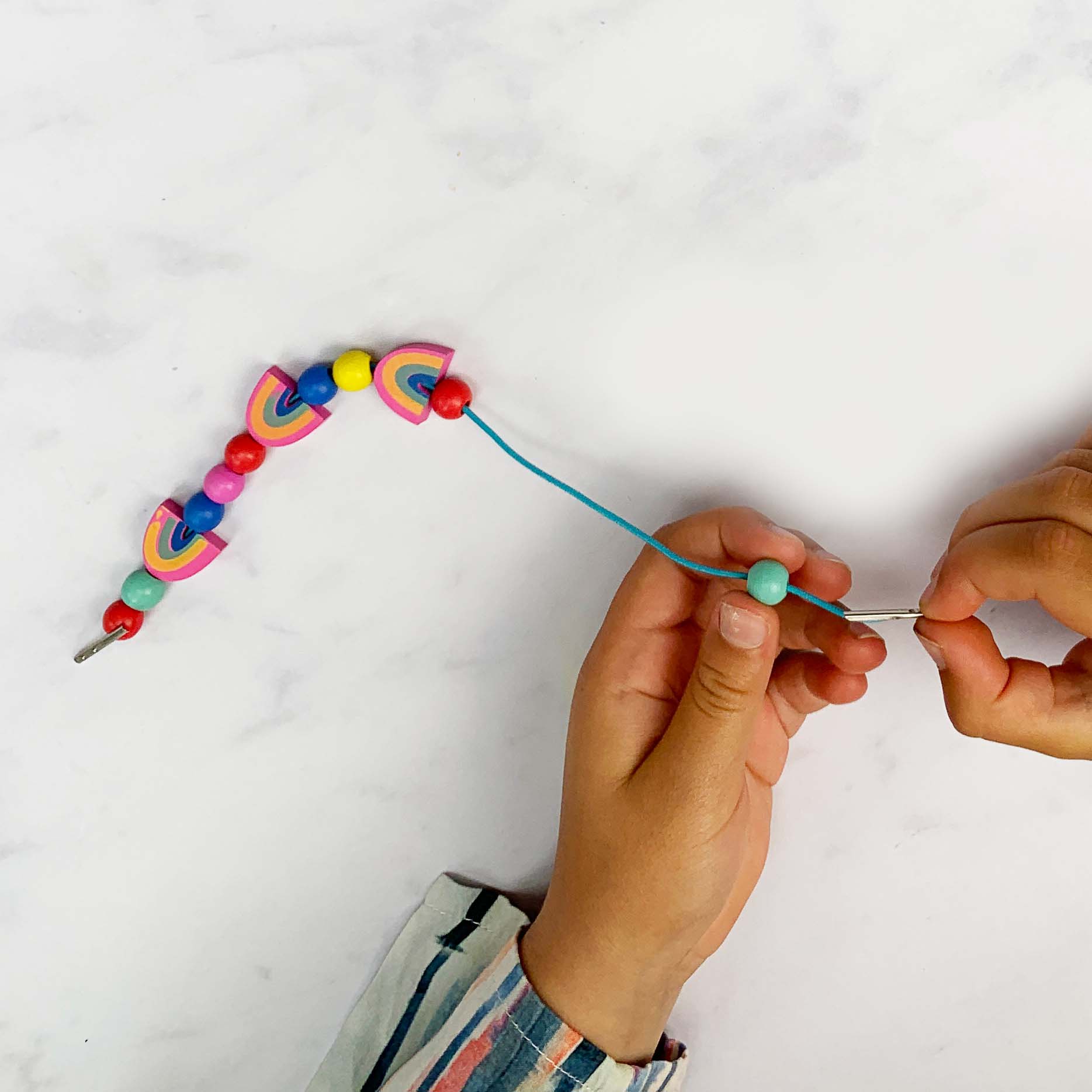 Child threading colourful beads, including rainbows, onto a blue elastic cord.