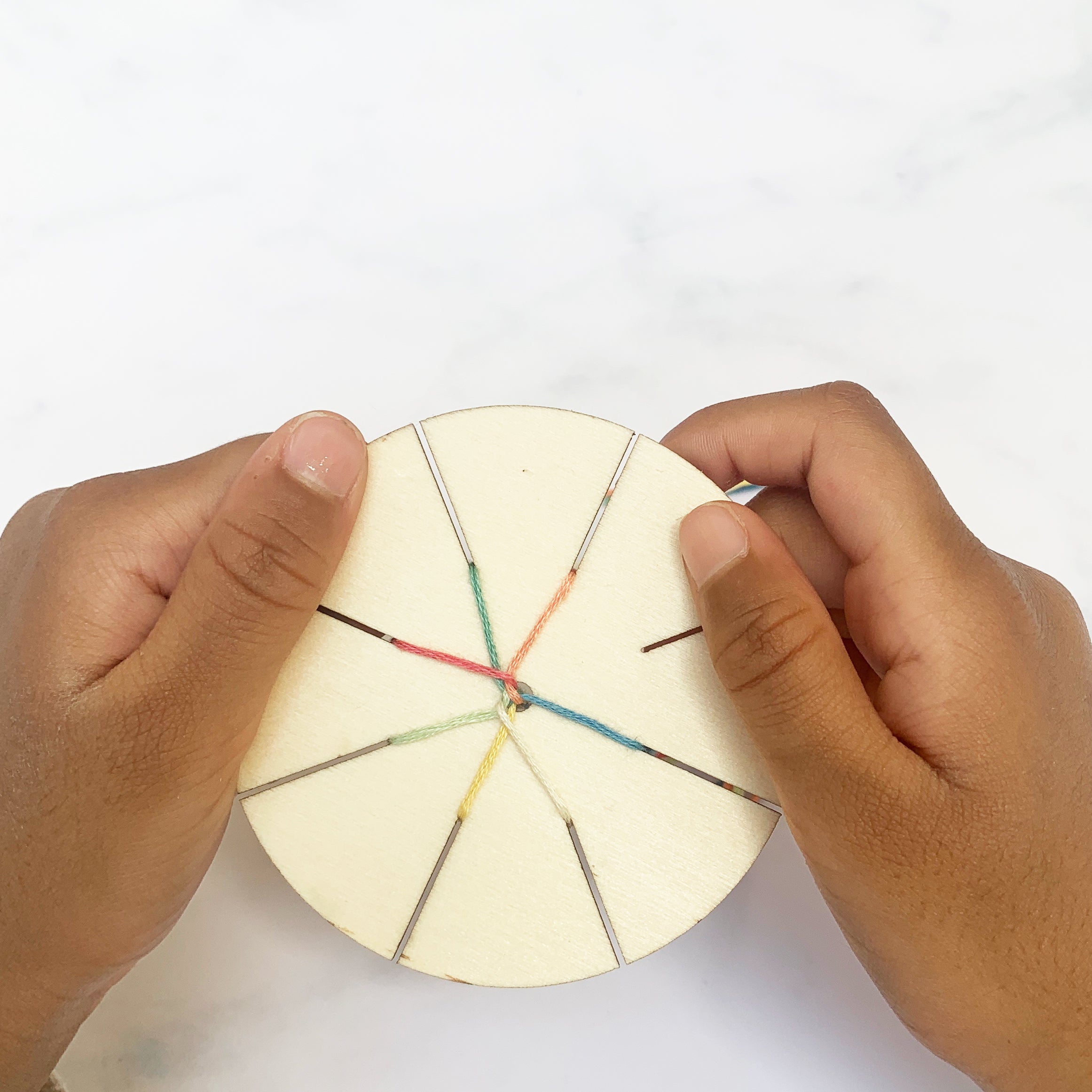 Child weaving a friendship bracelet using the wooden tool and colourful threads