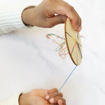 Child weaving a friendship bracelet using the wooden tool and colourful threads