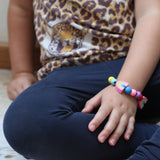 Child wearing a rainbow bracelet made from the kit, seated with legs crossed.