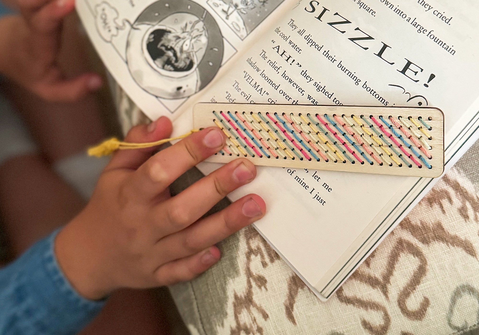 Child using cross-stitched wooden bookmark in a book